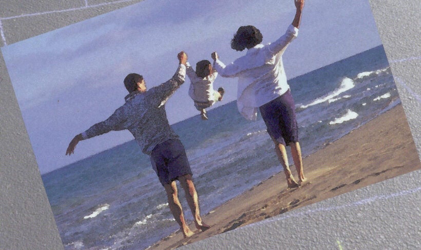 A mother and father walking on a beach holding hands of their toddler between them