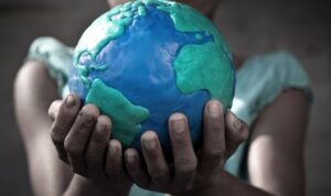 Hands outstretched toward us holding a model of planet earth made in clay.