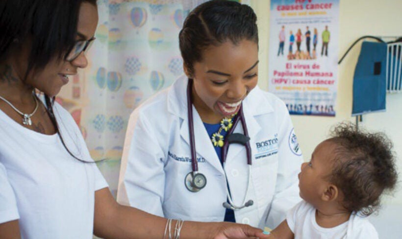 A smiling doctor interacting with an infant while the mother observes