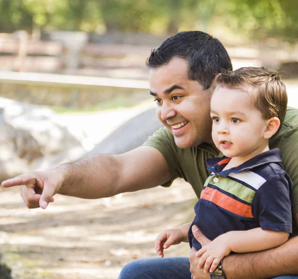 A smiling father holding his toddler and pointing to something off-camera