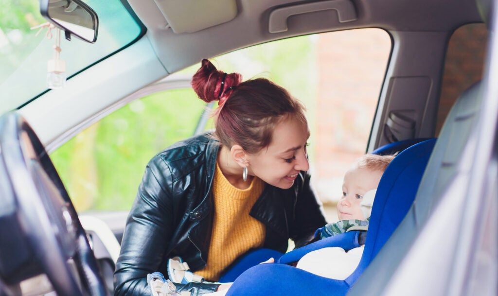 Smiling mother securing her baby into and infant car seat