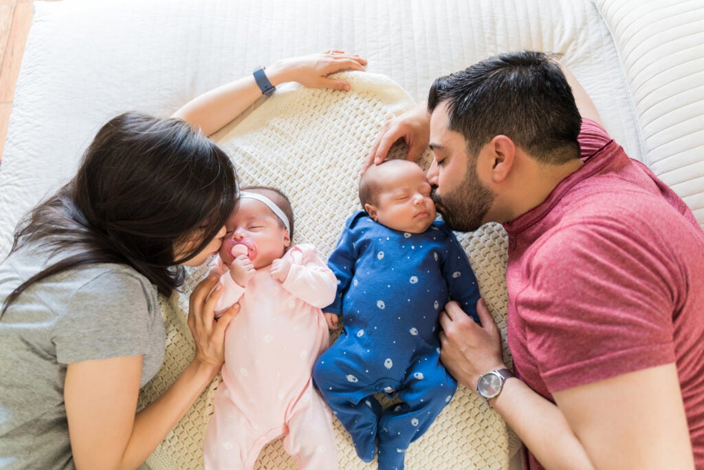 Infant twins, one being kissed by the mother, and one being kissed by the father