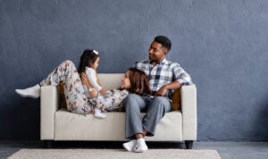 Smiling interracial parents sitting on a sofa and playfully interacting with their toddler daughter