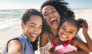 3 generations of women smiling and taking a selfie on a beach
