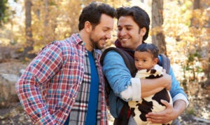 Gay couple in a fall woodland setting with their infant snuggled in one's arms