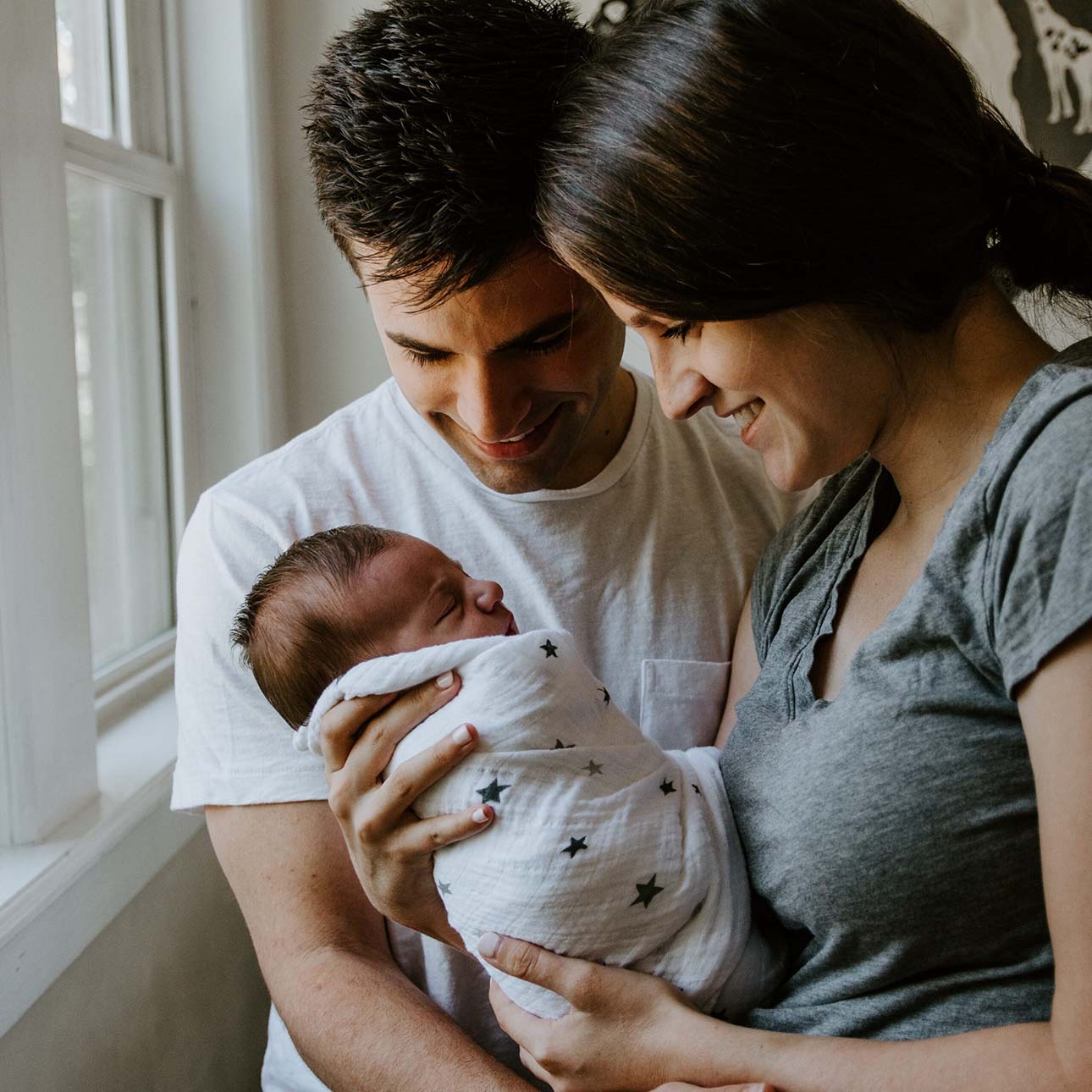 Happy new parents holding each other as the mother holds and smiles at her newborn infant